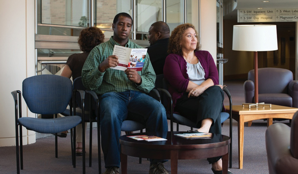 Image of a young man and a middle-aged woman sitting in a waiting room. The man is reading a pamphlet and the woman has her legs crossed and looking up.