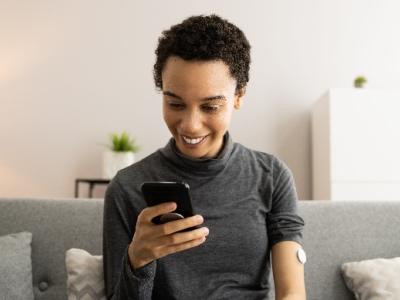 A woman seated with a glucose monitor on her left arm, checking her readings on her phone.